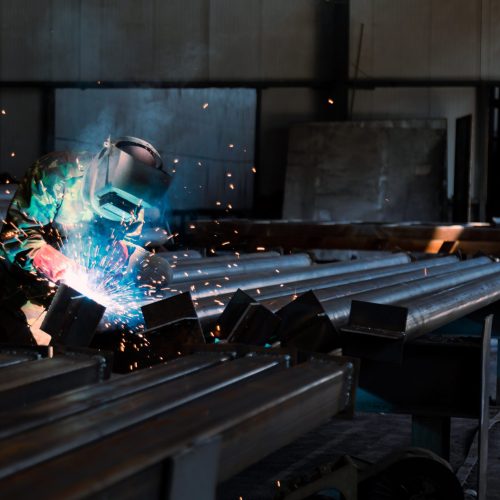 Industrial welder with a torch and protective helmet welding metal profiles in factory