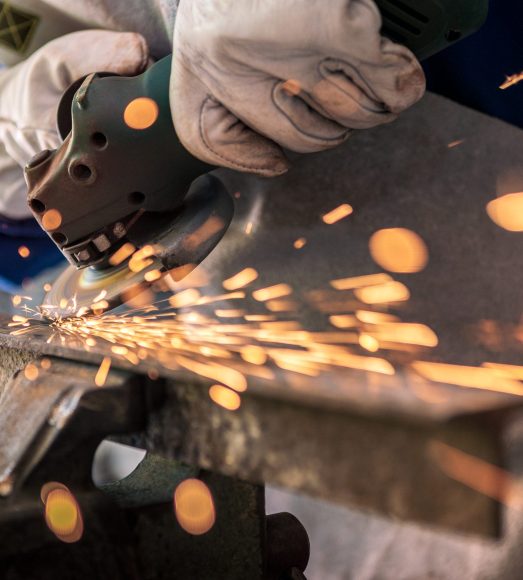Worker grinding metal with a grinder and cleaning the steel seam. Working in a metal processing workshop. The man works with an electric tool. Sparks from metal heating.