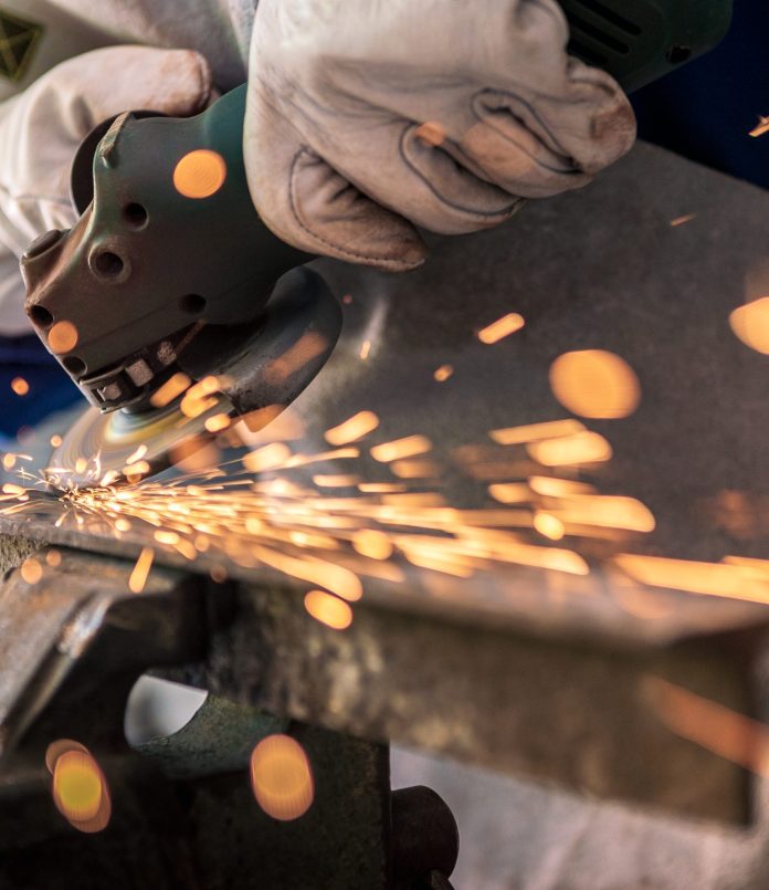 Worker grinding metal with a grinder and cleaning the steel seam. Working in a metal processing workshop. The man works with an electric tool. Sparks from metal heating.